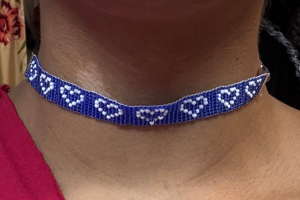 A close-up of a person wearing a blue beaded choker necklace with white heart patterns, paired with a red one-shoulder top.