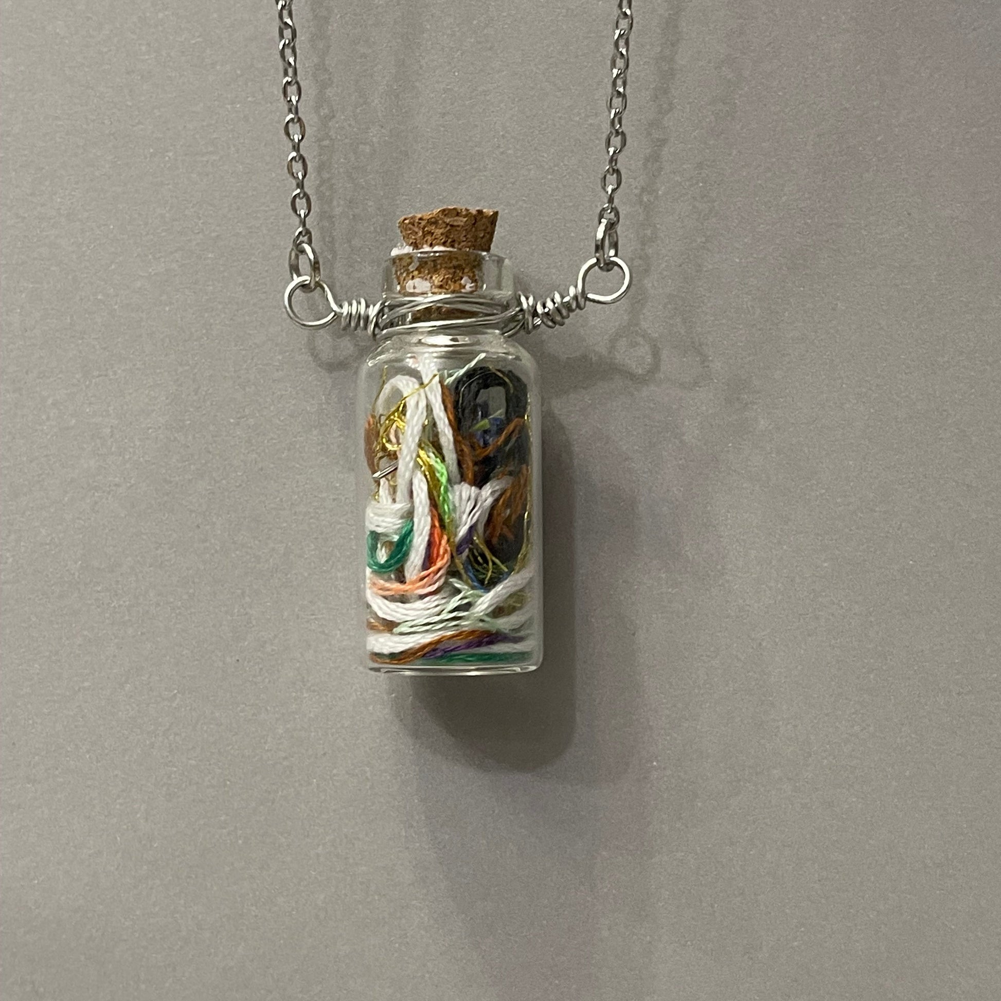 Glass bottle pendant with a small figurine on a gray background