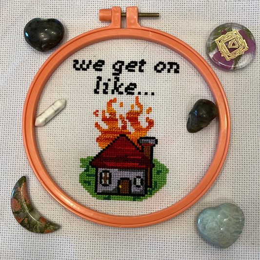 A cross-stitch pattern depicting a house with flames and the phrase 'we get on like.