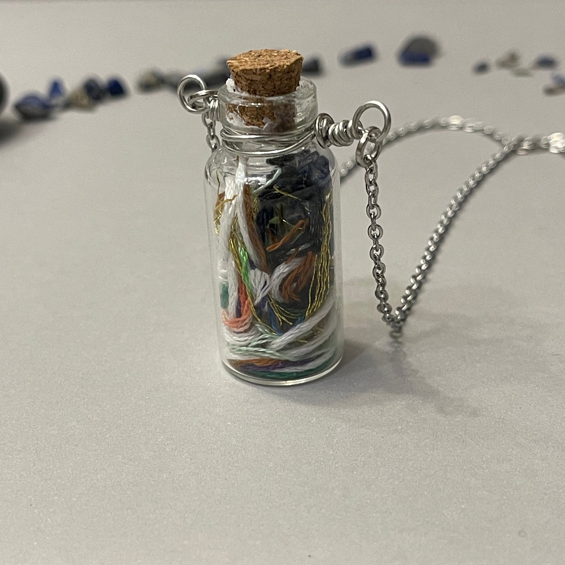 Glass bottle pendant with cork lid on a chain against a neutral background
