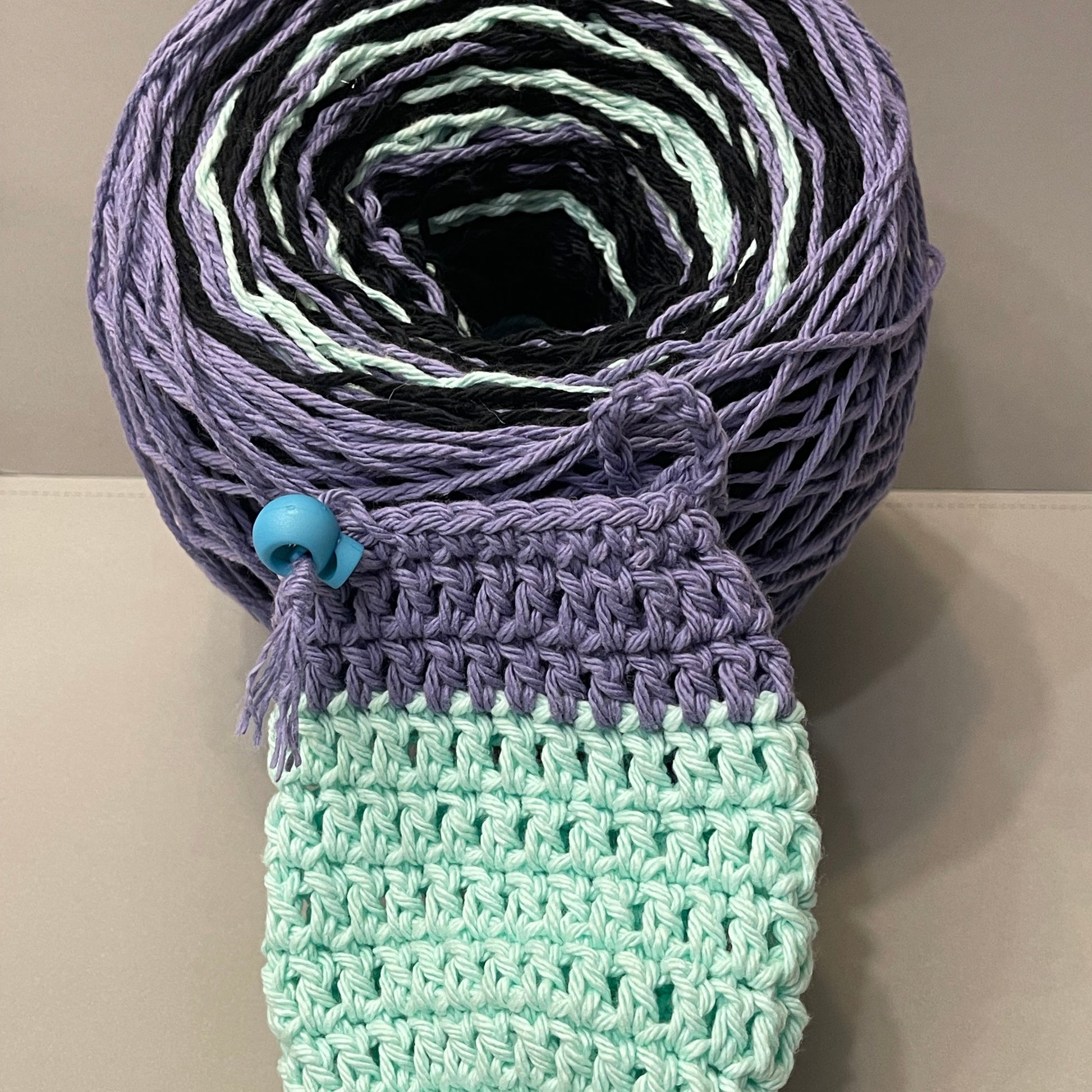 Spool of multicolored yarn with a crocheted item on a neutral background