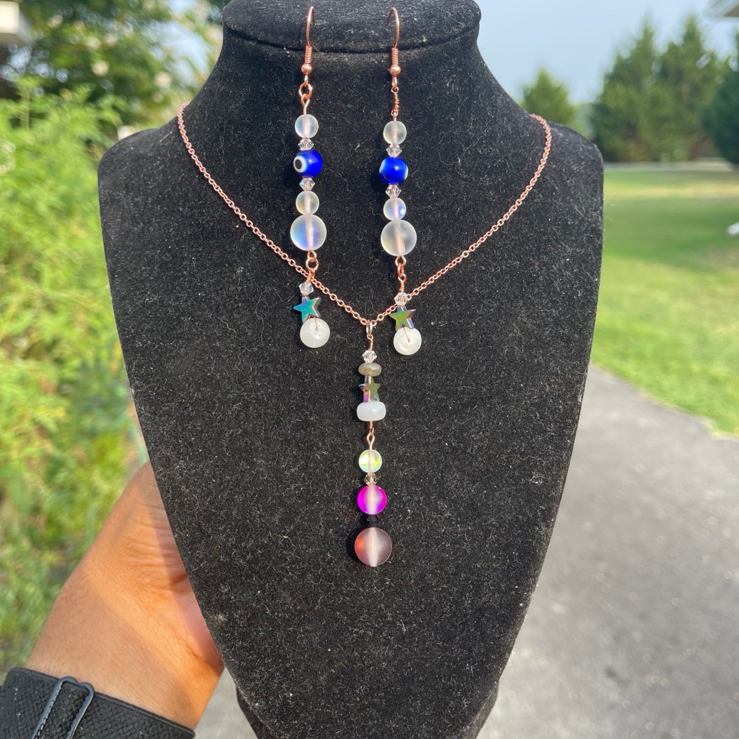 A set of copper galaxy earrings and necklace displayed on a mannequin. The earrings have a rose gold plated hook and the necklace features a rose gold chain.