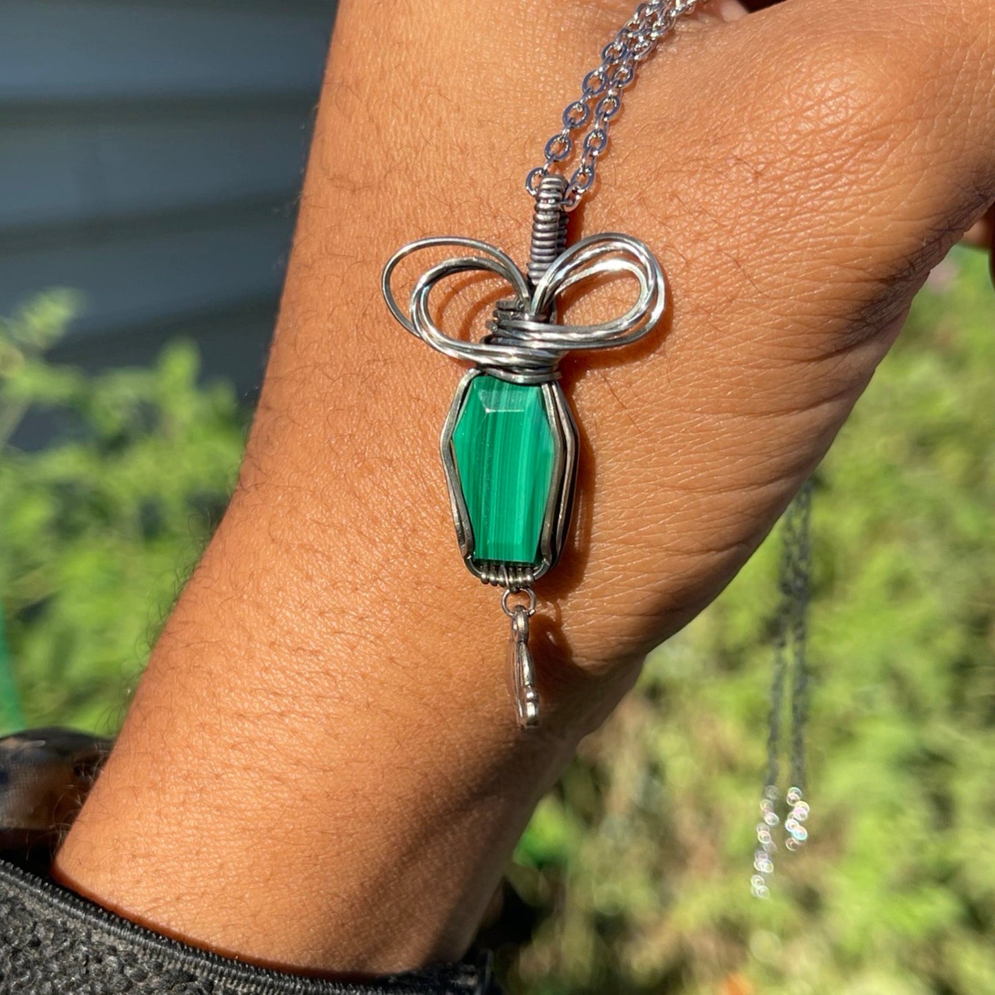 A sterling silver Malachite Coffin Pendant with a green gemstone, wrapped in silver wire and presented on a chain.