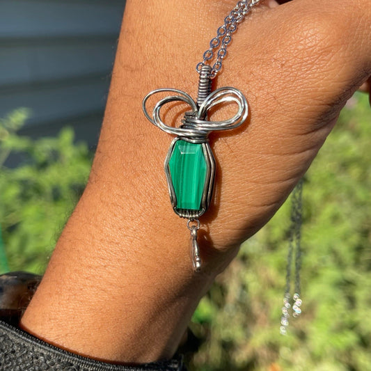 A sterling silver Malachite Coffin Pendant with a green gemstone, wrapped in silver wire and presented on a chain.