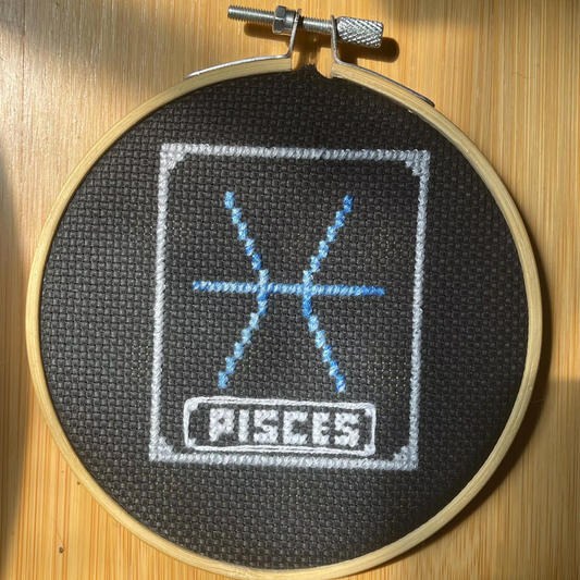 Embroidery hoop with 'Pisces' design on a wooden surface