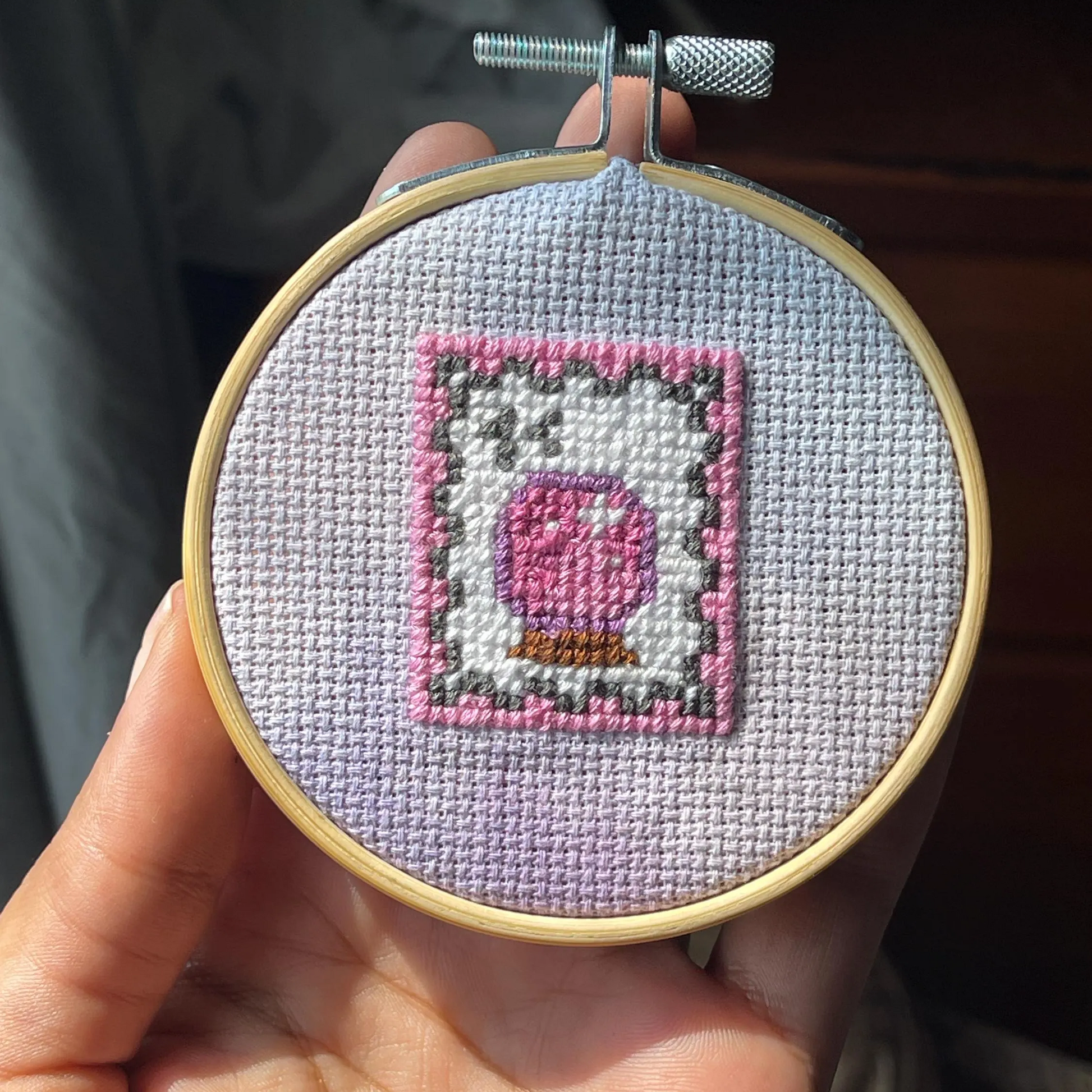 Cross-stitched piece in a hoop held by a person