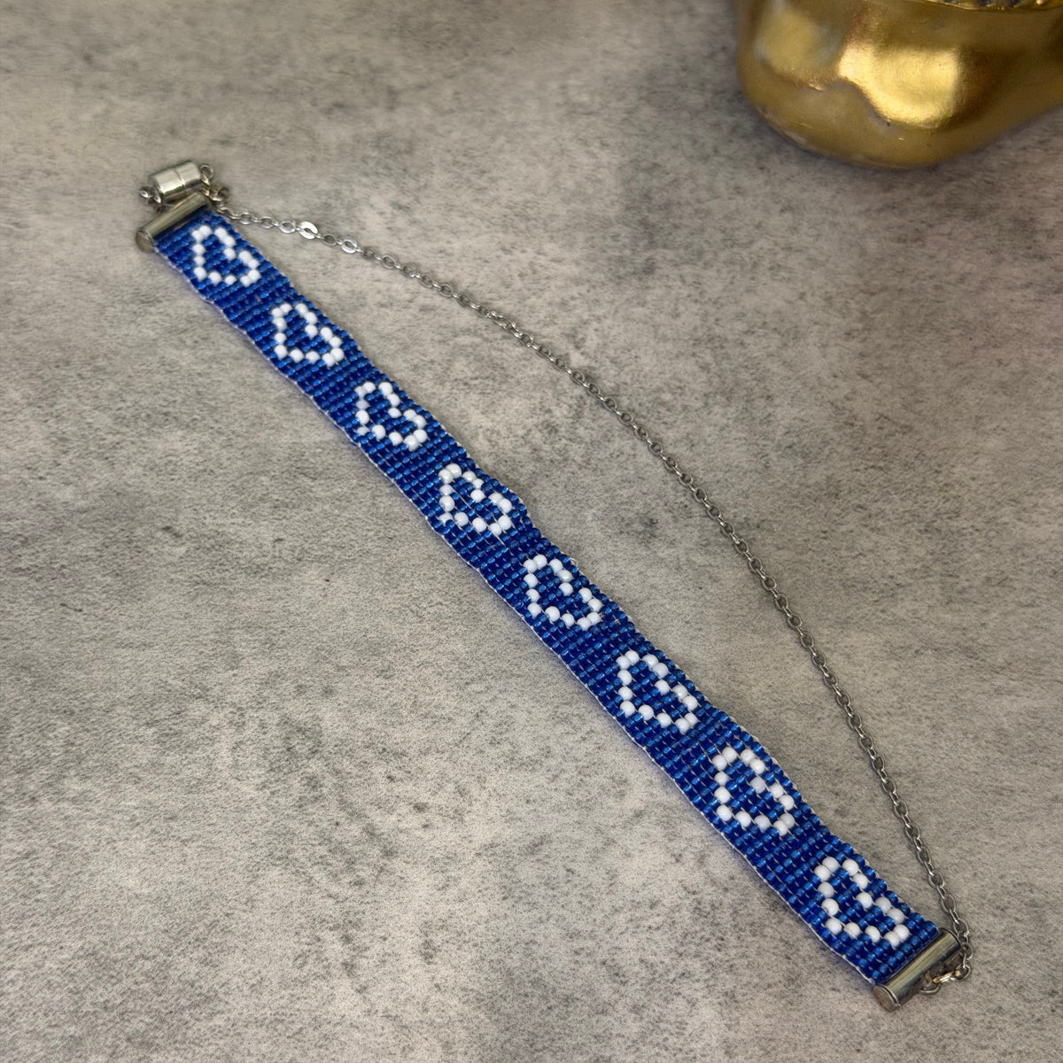 A beaded bracelet with a blue and white geometric pattern, featuring a silver-toned chain extender and clasp, displayed on a textured gray surface.