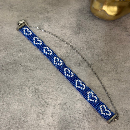 A beaded bracelet with a blue and white geometric pattern, featuring a silver-toned chain extender and clasp, displayed on a textured gray surface.