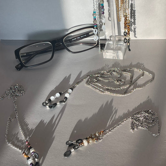 Jewelry and eyeglasses on a gray surface with a clear stand.