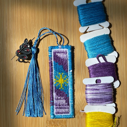 Handmade bookmark with blue tassel and colorful thread spools on a wooden surface